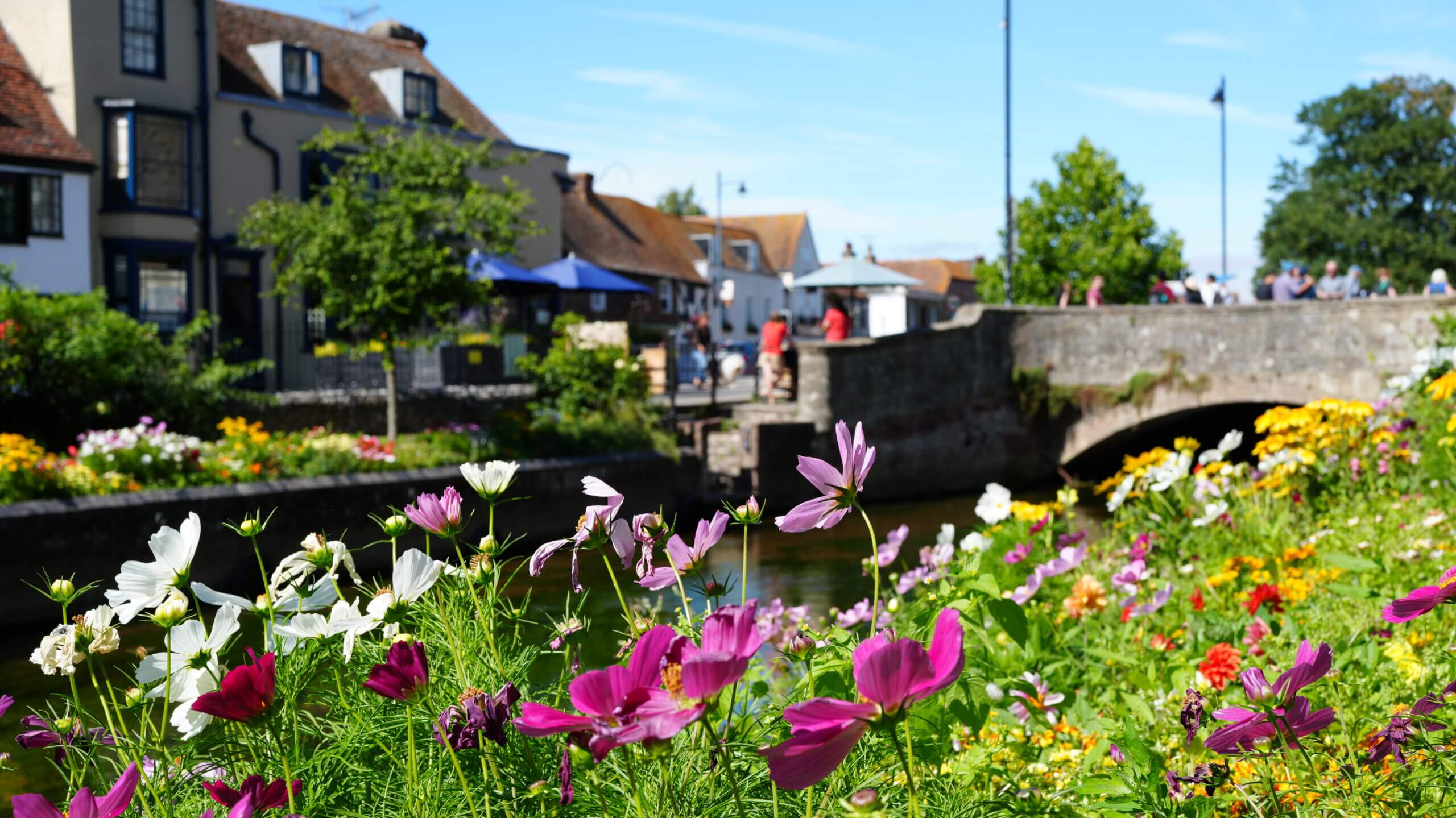 Colourful summer flowers beside the River Stour and a historic bridge in Canterbury city centre.