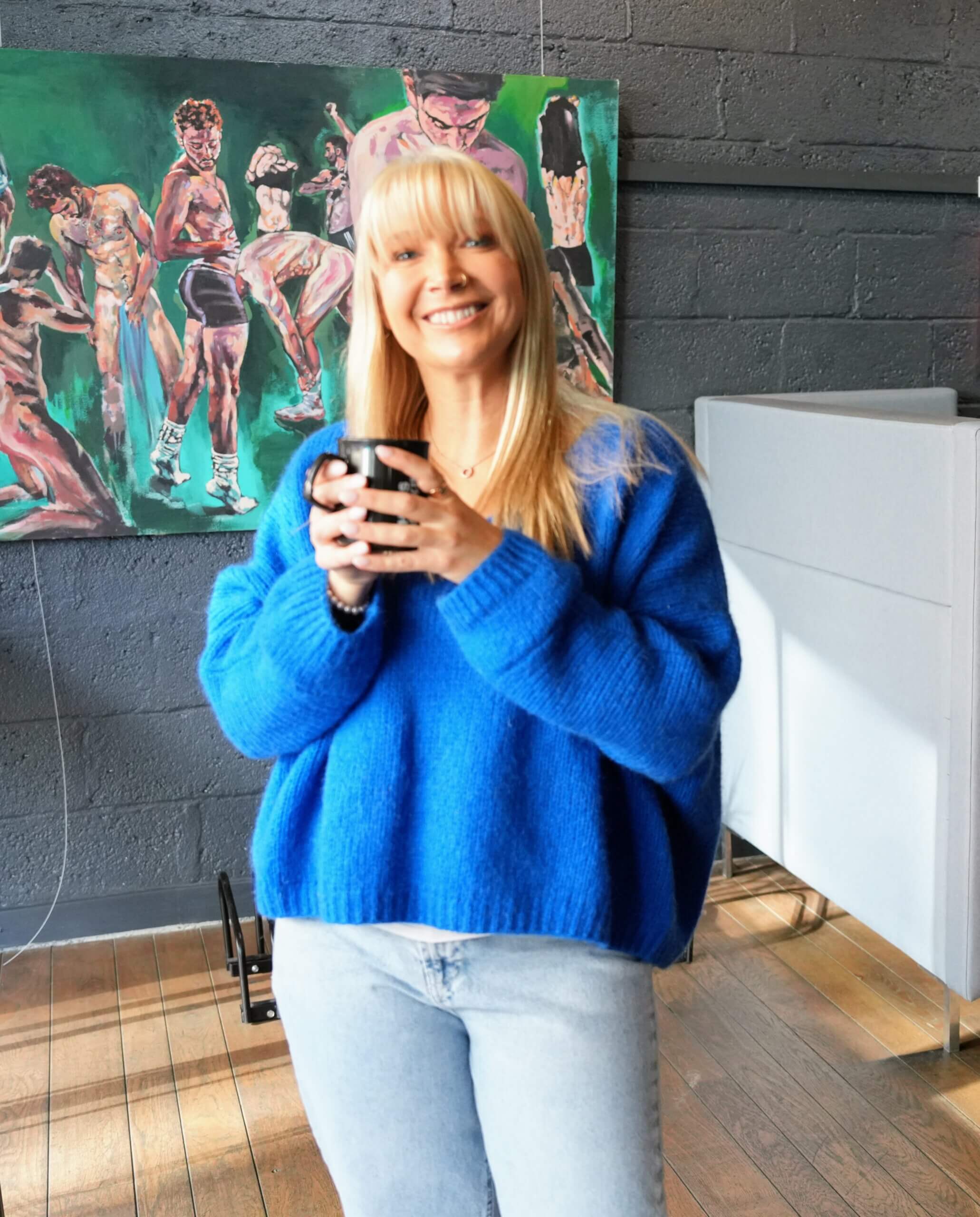 Becky from Home From Home Canterbury holding a cup of coffee and smiling in a welcoming indoor setting.