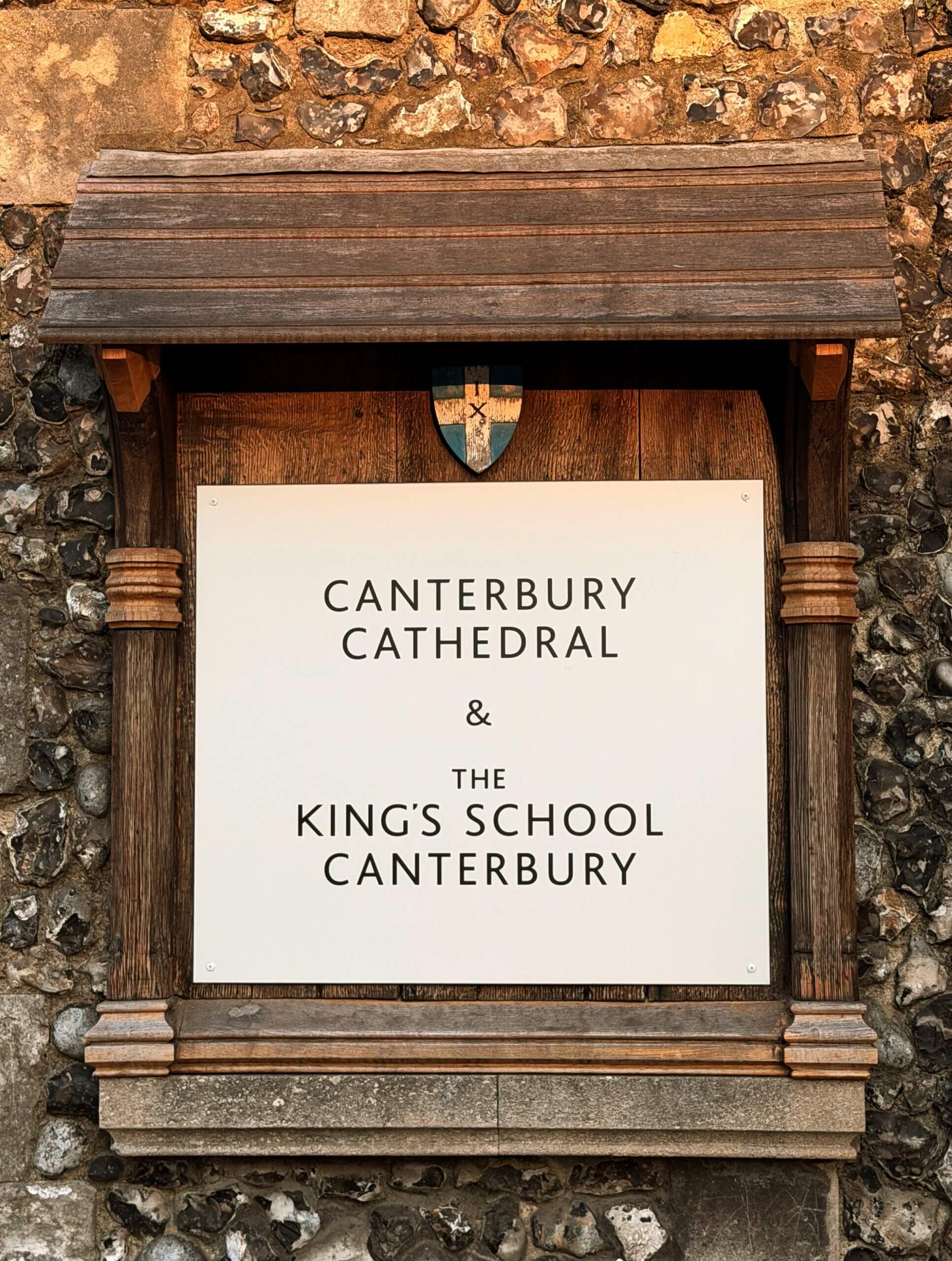 Entrance sign for Canterbury Cathedral and The King's School Canterbury mounted on a historic flint stone wall.