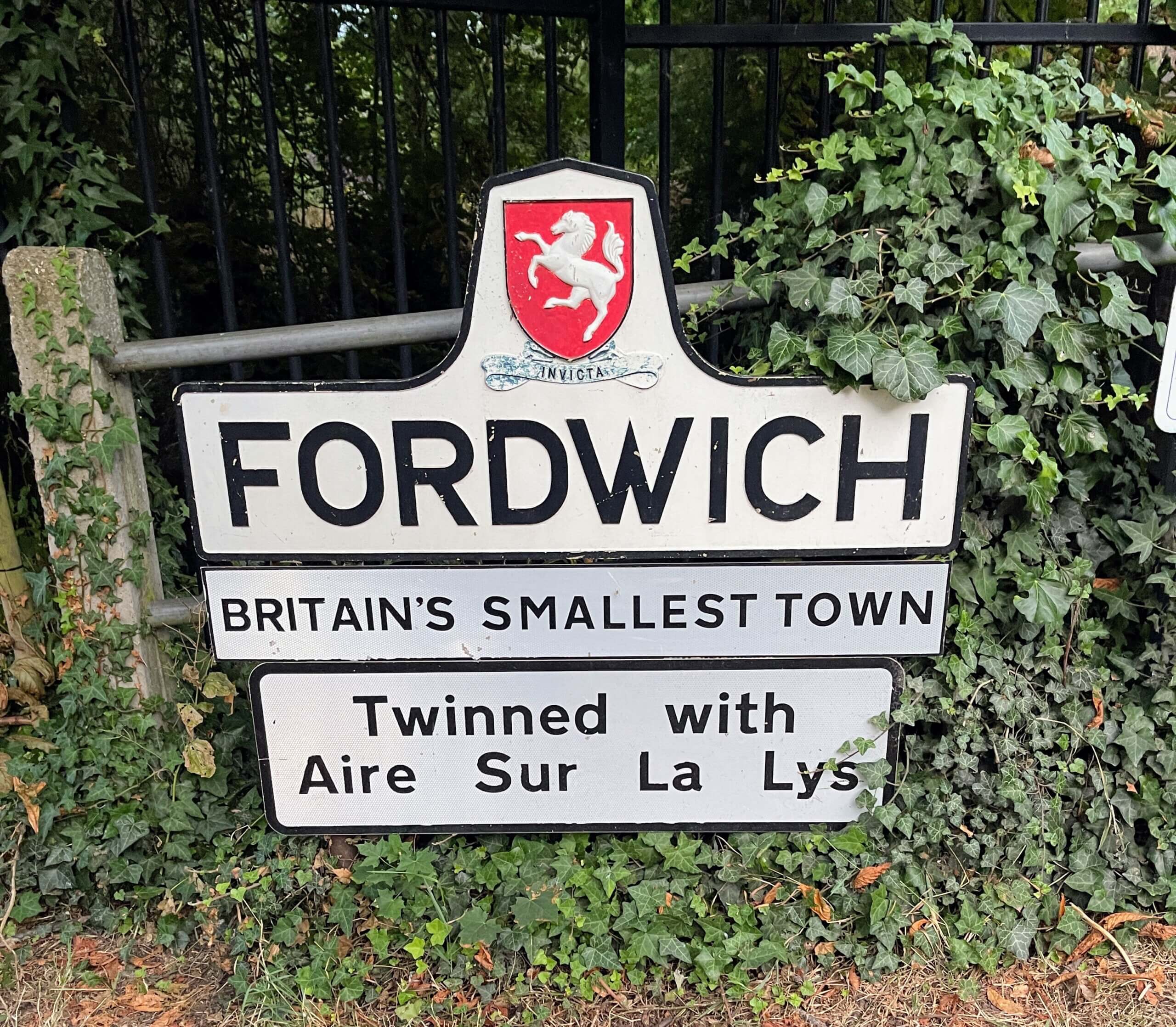 A welcome sign for Fordwich, Britain's smallest town, surrounded by green ivy and trees at the town entrance.
