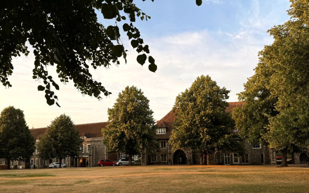Historic lawn and school buildings at The King's School Canterbury surrounded by mature trees at sunset.