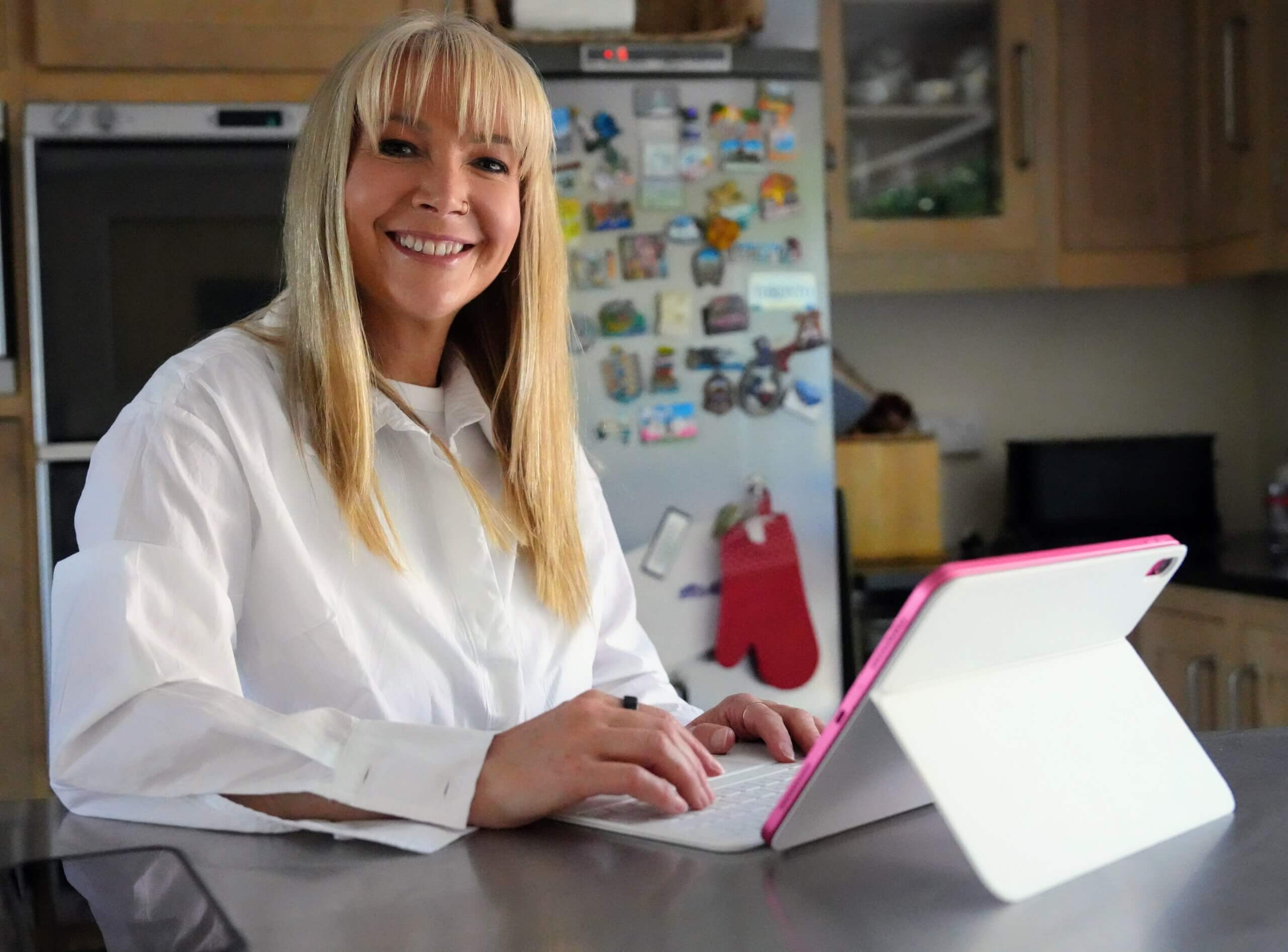 Rebecca Stone smiles while using a tablet at a kitchen table, reflecting her approachable and supportive role as a local guardian in Canterbury.