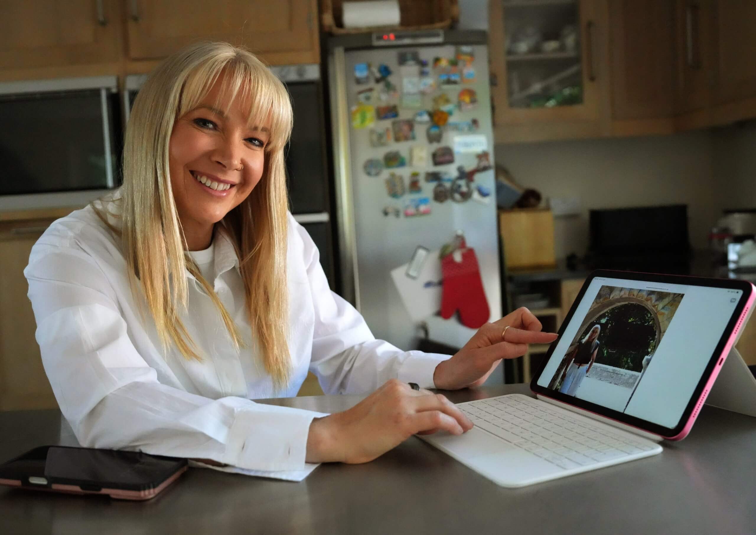 Rebecca Stone smiles while using a tablet at her kitchen table, showcasing the personal and approachable support she provides as a local guardian in Canterbury.